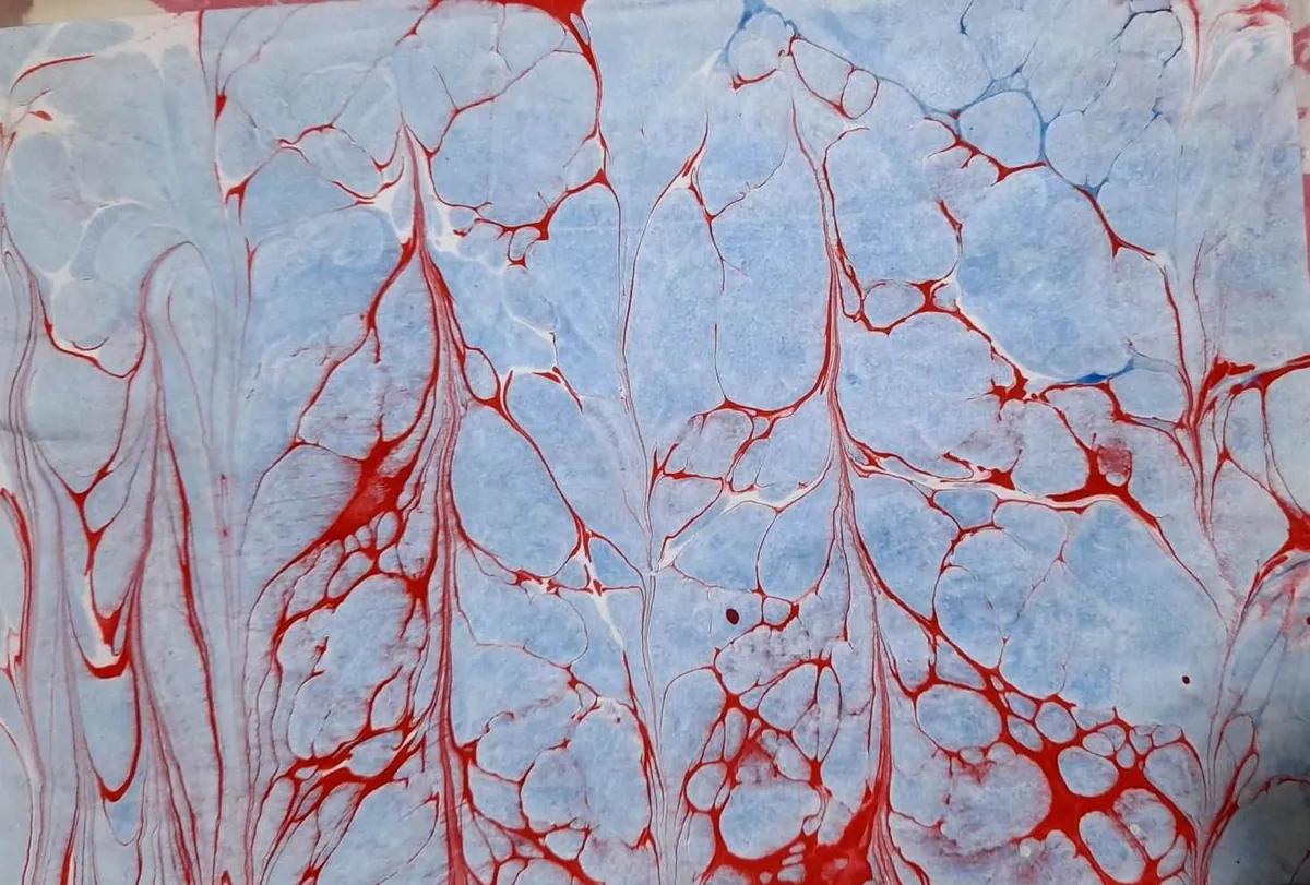 Muestra EBRU con vetas rojas sobre un fondo celeste