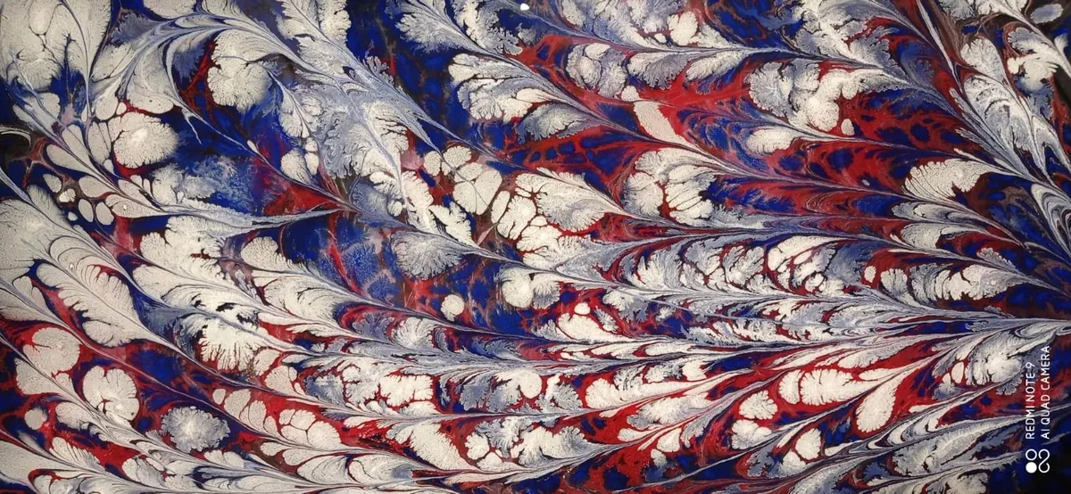 Pintura sobre agua con formas blancas, azules y rojas entrelazadas